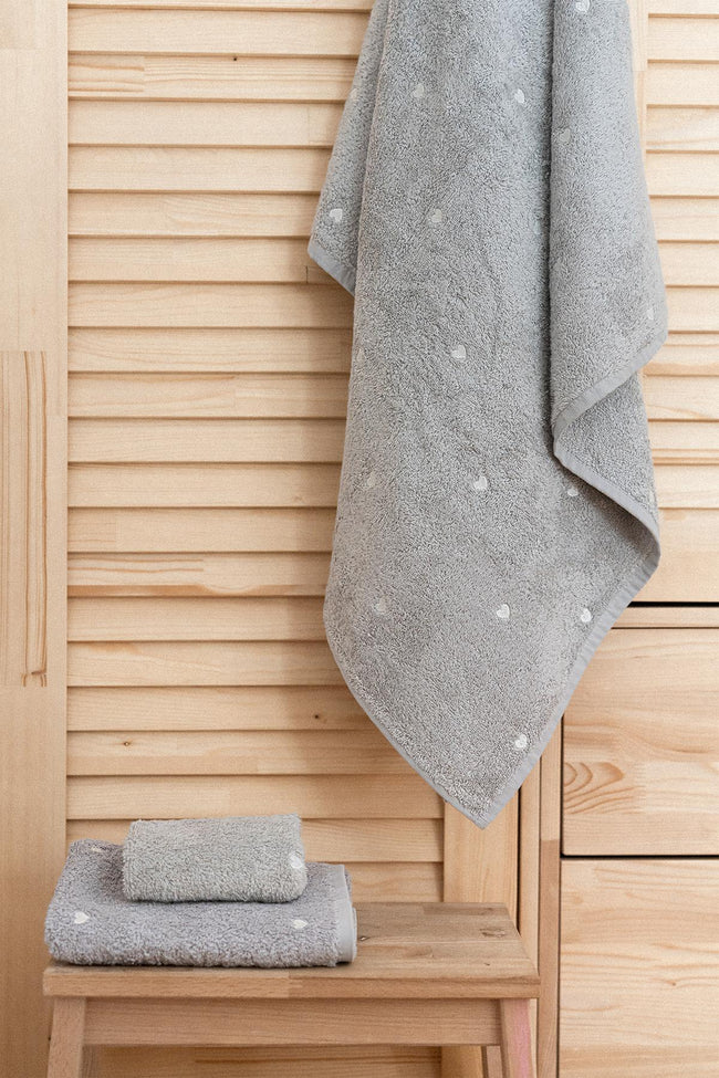 Gray high-quality bath towel with white heart pattern, displayed on a wooden floor
